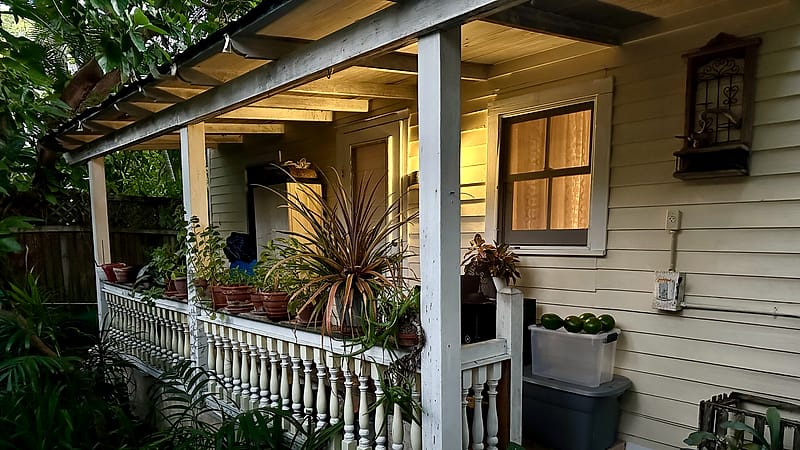 A partly built wooden deck attached to the rear of a house, with framing exposed and lumber stacked on the lawn