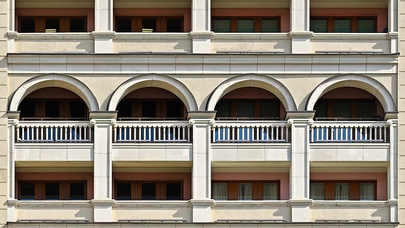 A modern hotel exterior of glass and pale stone photographed at an angle, with an unbranded canopy over the entrance drive