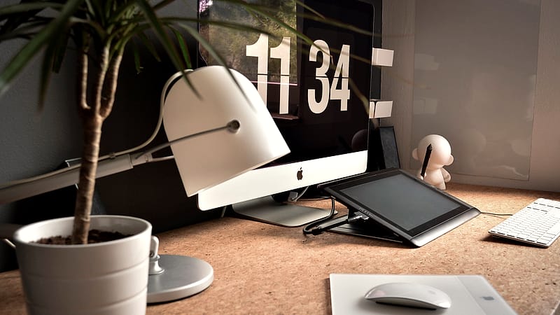 A hand holding a small security key device beside a laptop keyboard on a desk in a quiet office