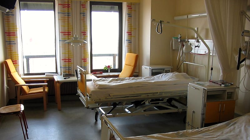 A quiet hospital nursery corridor with a row of empty bassinets and soft light through a wide window