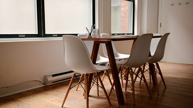 Two pens lying across a single printed page on a bare conference table with two empty chairs behind it