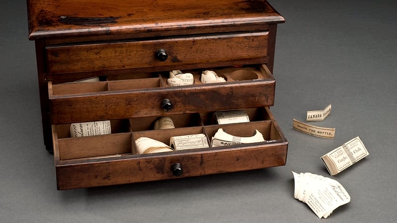 Close view of amber glass vials and blister strips arranged in labeled compartments inside a wooden drawer