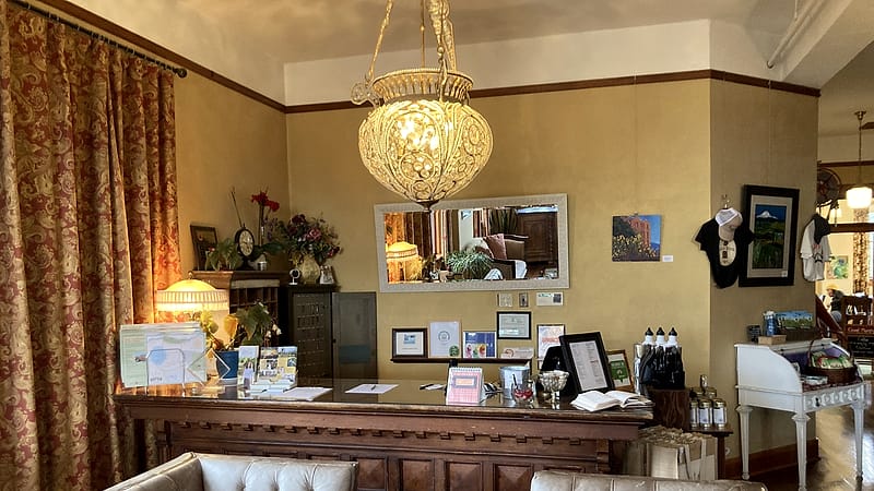 A quiet hotel reception counter of dark wood with a small bell, a closed ledger and warm lamps behind an empty lobby