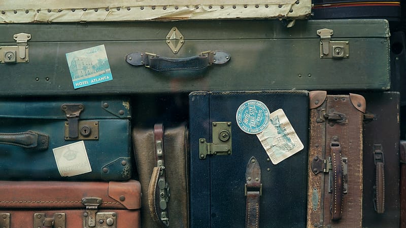 Several closed suitcases and a canvas bag stacked on a luggage cart in a bare storage room with a metal shelf