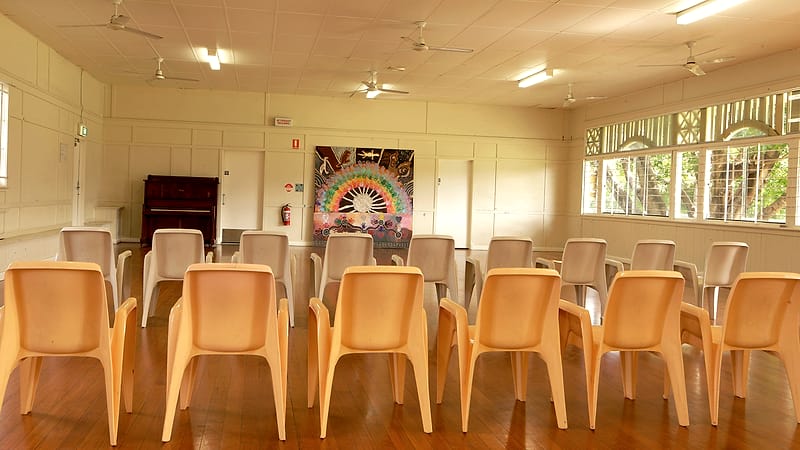 Five empty chairs behind a long table with name placards and water glasses in a community meeting room