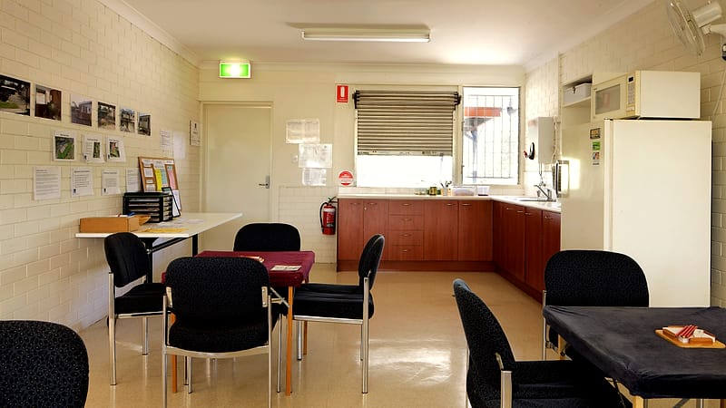 An empty community clubhouse meeting room with stacked chairs facing a folding table and a projector screen