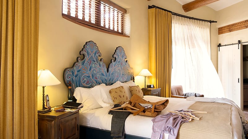 A studio-style extended-stay room with a small kitchenette, a two-seat table and a made bed lit by a wide window