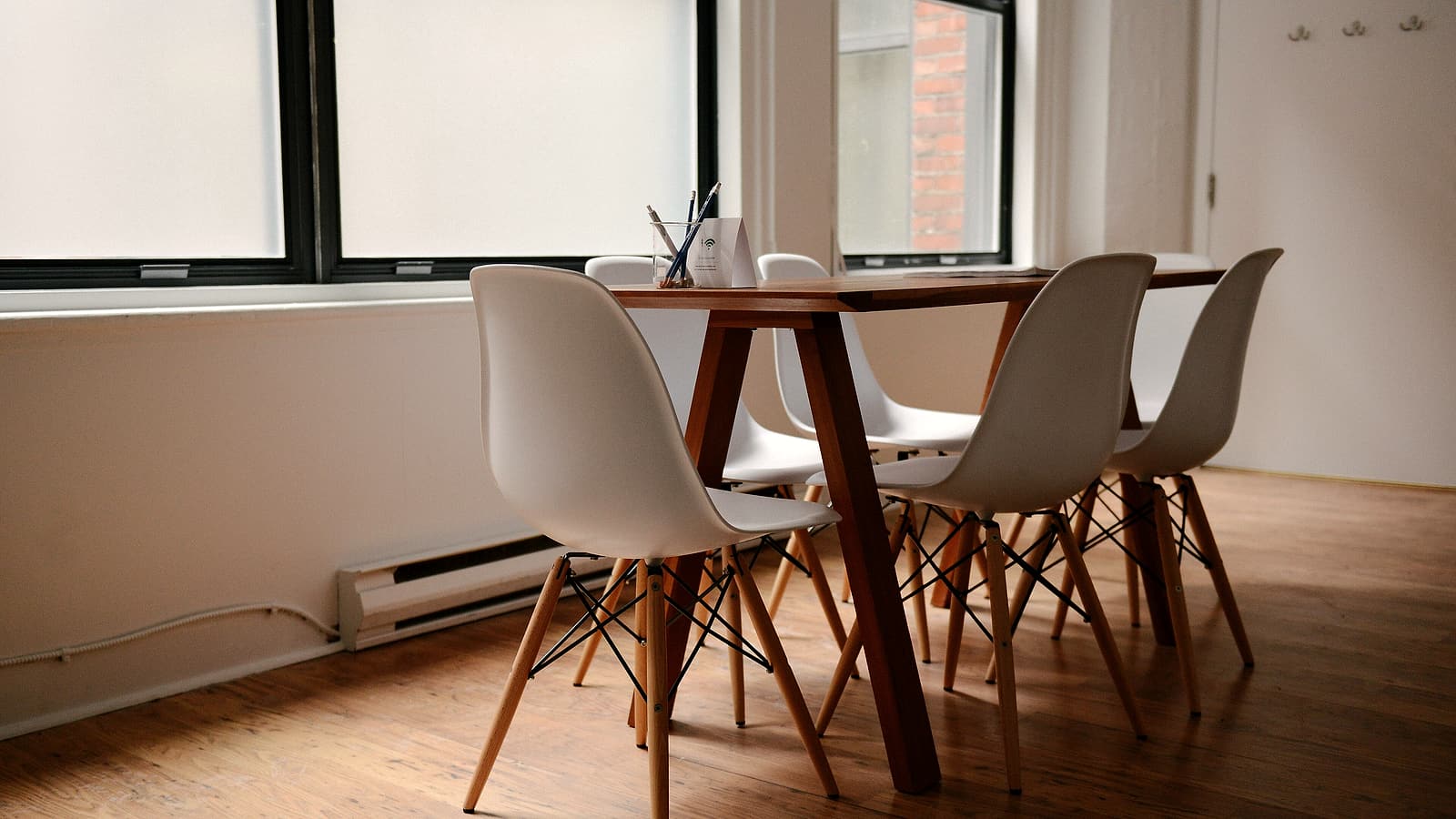 Two pens lying across a single printed page on a bare conference table with two empty chairs behind it