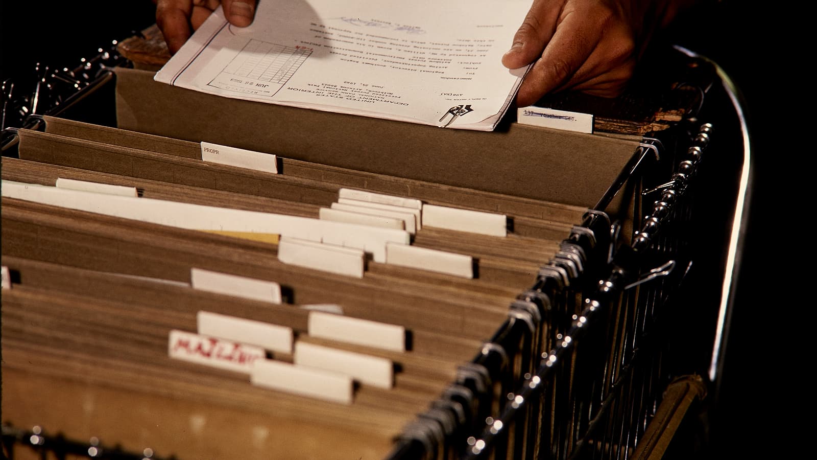 A stack of printed pages held together by a metal clip resting on a wooden desk beside a pair of reading glasses