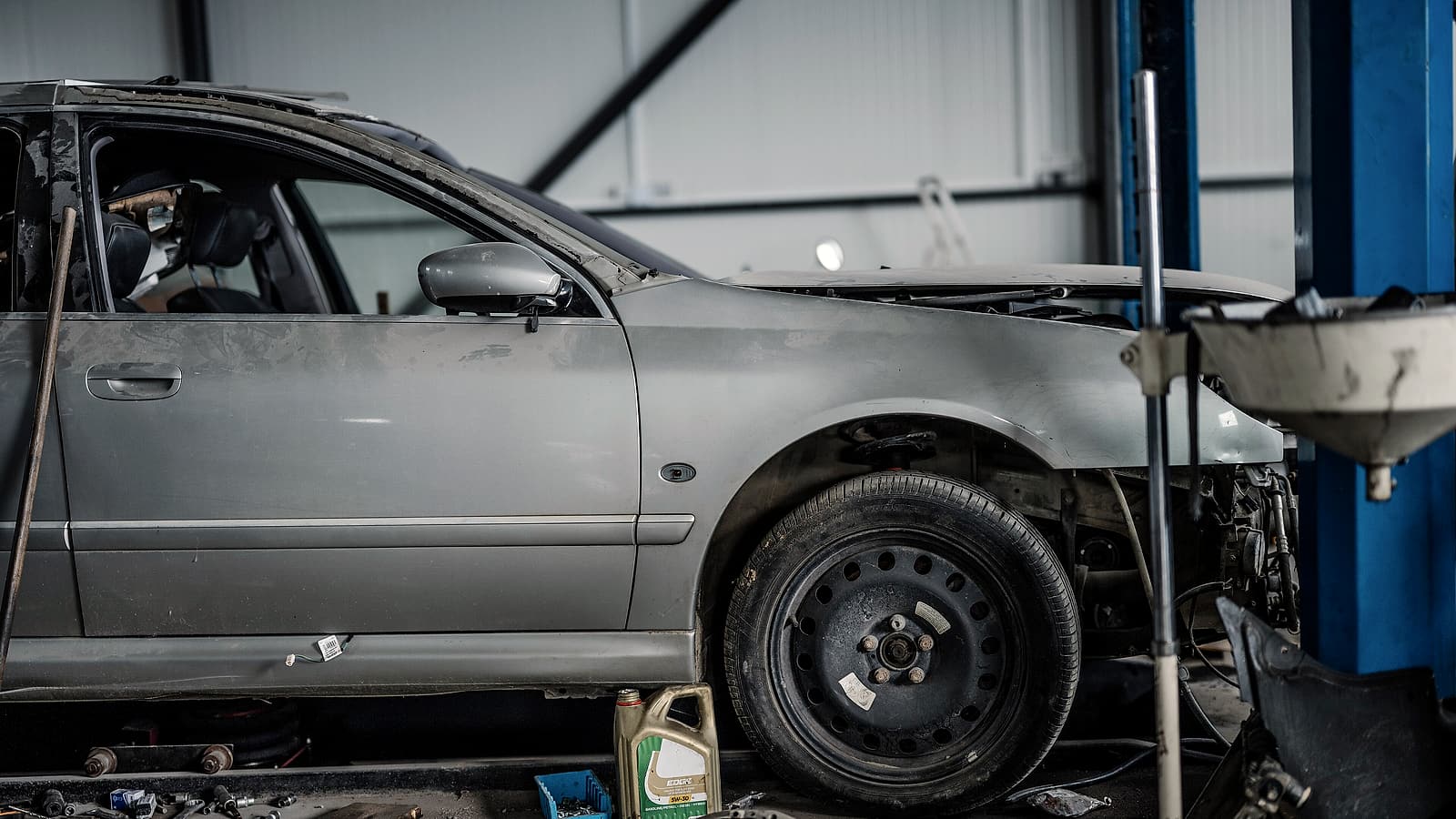 A car raised on a two-post lift inside a repair bay with tools on a rolling cart and a workbench along the wall
