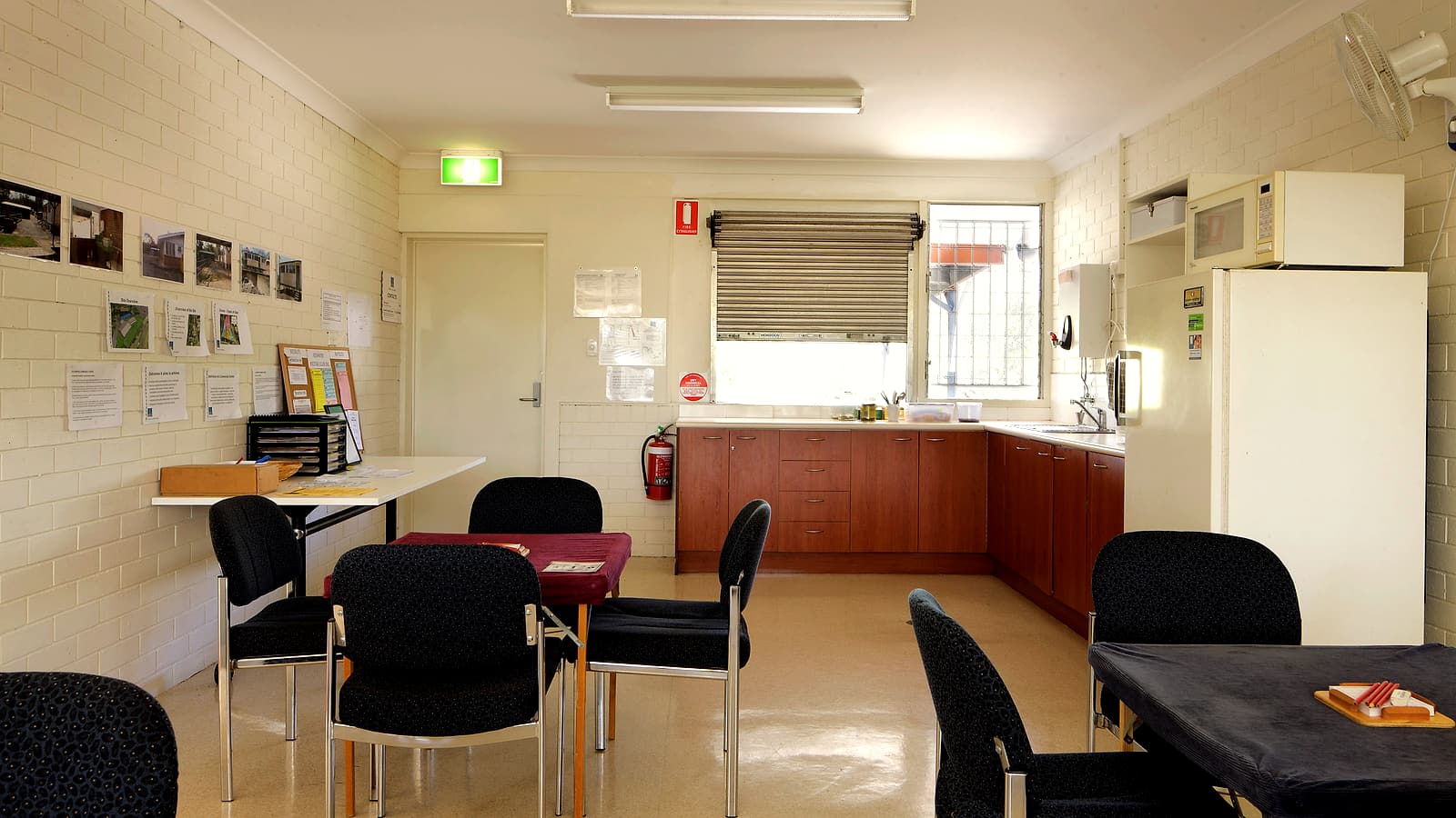 An empty community clubhouse meeting room with stacked chairs facing a folding table and a projector screen